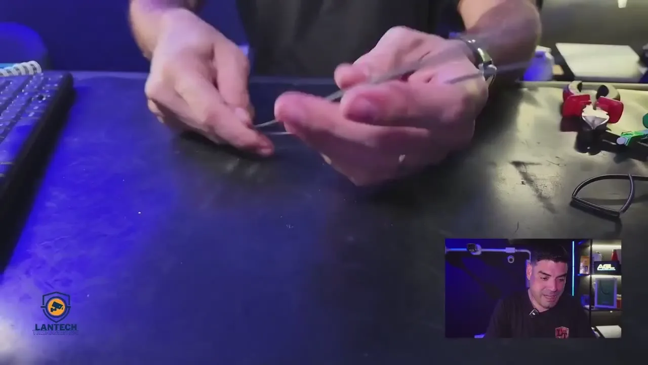 Mãos na bancada separando o arame de sustentação do cabo drop de fibra óptica, com as ferramentas do kit ao lado